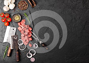 Raw lean diced casserole beef pork steak with vintage meat hatchet and fork on stone background. Salt and pepper with fresh