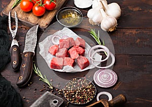 Raw lean diced casserole beef pork steak with vintage meat hatchet and knife and fork on wooden background. Salt and pepper with