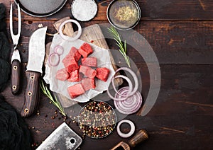 Raw lean diced casserole beef pork steak with vintage meat hatchet and knife and fork on wooden background. Salt and pepper with