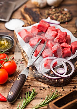 Raw lean diced casserole beef pork steak with vintage meat hatchet and knife and fork on wooden background. Salt and pepper with
