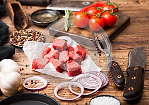 Raw lean diced casserole beef pork steak with vintage meat hatchet and knife and fork on wooden background. Salt and pepper with