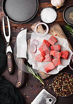 Raw lean diced casserole beef pork steak with vintage meat hatchet and knife and fork on wooden background. Salt and pepper with