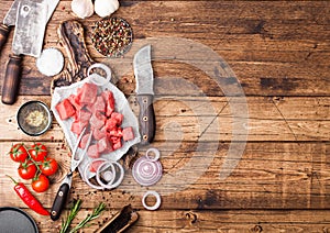 Raw lean diced casserole beef pork steak with vintage meat hatchet and knife on wooden background. Salt and pepper with fresh