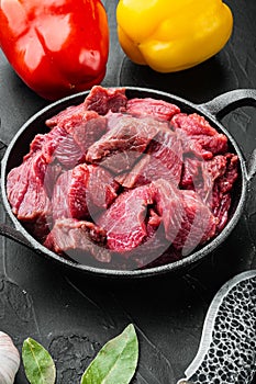 Raw lean stewing beef with sweet bell pepper, in cast iron frying pan, on black stone background