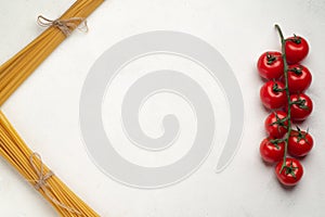 Raw long pasta and a branch of cherry tomatoes symmetry top view free space