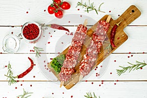 Raw lula kebab on skewers with spices on wooden board