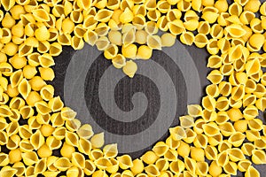 Raw macaroni - conchiglie paste shells. In the middle of the empty space in the shape of a heart on a black background