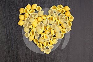Raw macaroni - conchiglie paste shells in the shape of a heart on a dark background