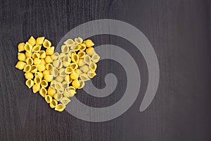 Raw macaroni - conchiglie paste shells in the shape of a heart on a dark background