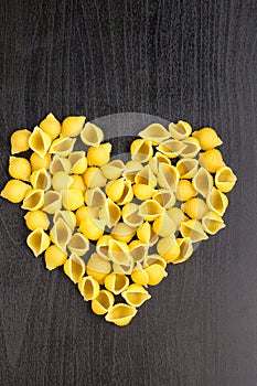 Raw macaroni - conchiglie paste shells in the shape of a heart on a dark background