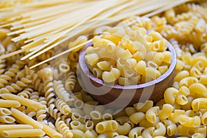 Raw macaroni on wooden bowl, pasta various kinds of uncooked pasta spaghetti and noodles on background, Italian food culinary