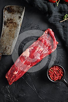 Raw machete also known as bistro steak, fajita meat or onglet, near butcher knife with pink pepper and rosemary. Black background