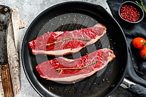 Raw marbled beef steak on a grill pan, ingredients for cooking. Gray background. Top view