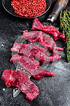 Raw marbled meat cut into thin strips for beefstroganoff. Black background. Top view