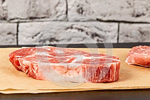 raw marbled meat pork steak on brown parchment paper on black table against gray brick wall background