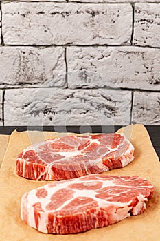 raw marbled meat pork steak on brown parchment paper on black table against gray brick wall background
