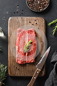 Raw marbled ribeye steak with rosemary sprig on cutting board. Vertical composition