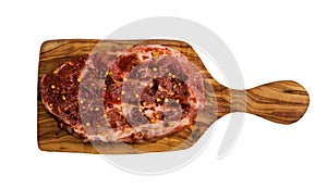 Raw marinated pork steak with red pepper flakes, on cutting board made from olive wood. Isolated on white background, top view