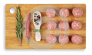 Raw meat balls on a chopping board. Rosemary, chili pepper, spices. White background. Top view