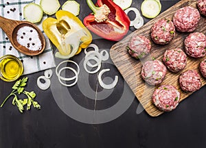 Raw meat balls with herbs and onions on a cutting board with bell peppers, butter, on wooden rustic background top view