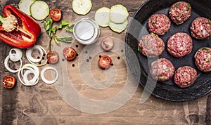 Raw meat balls in vintage cast-iron pan with tomatoes, onions and peppers, herbs on wooden rustic background top view close up