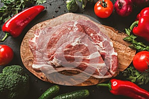 Raw meat, beef steak on cutting board on black background with ingredients for cooking
