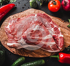 Raw meat, beef steak on cutting board on black background with ingredients for cooking.
