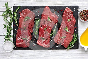 Raw meat, beef steak with spices, olive oil and rosemary on black slate cutting board over wooden background