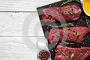 Raw meat, beef steak with spices, olive oil and rosemary on black slate cutting board over wooden background