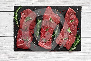 Raw meat, beef steak with spices and rosemary on black slate cutting board over wooden background