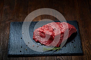 Raw meat beef steaks on black slate board with spices and rosemary over wooden background, copy space