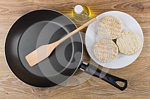 Raw meat cutlets in plate, bottle of oil, frying pan