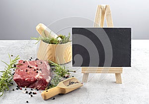 Raw meat with herbs and spices mortar on gray marbe background and with easel for text, top view, copy space