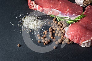 Raw meat and pepper. Close-up of two slices of fresh raw meat and a rosemary branch on a black slate stone plate. Preparing meat