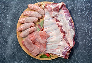 Raw meat products.Barbecue pork ribs, steaks, grilled sausages,minced meat, garnished with spices on a round wooden chopping board