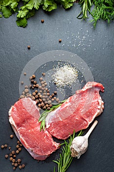 Raw meat salt and spices. Top view of fresh slices of raw meat, garlic, rosemary and spices on black slate stone plate. Preparing