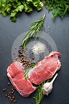 Raw meat salt and spices. Top view of slices of fresh raw meat, garlic, rosemary and spices on a black slate stone plate.