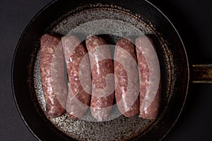 Raw meat sausages in a frying pan on a black background.