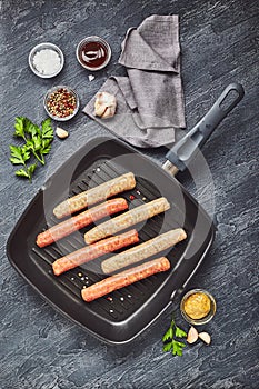 Raw meat sausages on a square grill pan, with herbs and spices.