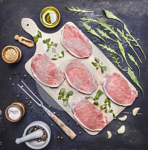 Raw Meat set Pork steaks with herbs and spices on a white cutting board wooden rustic background top view