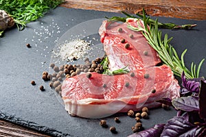 Raw meat with spices. Slices of fresh raw meat with salt, spices and herbs on a black slate stone plate. Preparing and marinating