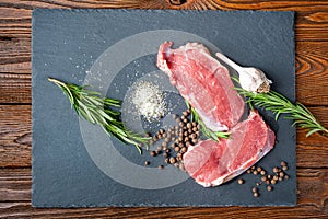 Raw meat and spices. Top view of two pieces of fresh raw meat, garlic, rosemary and spices on a black slate stone plate. Preparing