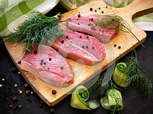 Raw meat, steak on a wooden Board. Spices, dill, peppers and roll of cucumber. Ready for cooking and roasting.