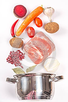 Raw meat, vegetables, beans and spices on a white background with a pan, top view