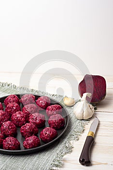 Raw meatballs with beetroot into a black baking tray