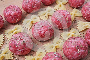 Raw meatballs and pasta bows on a wooden Board