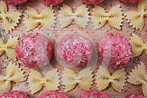 Raw meatballs and pasta bows on a wooden Board