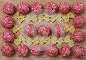 Raw meatballs and pasta bows on a wooden Board