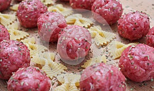 Raw meatballs and pasta bows on a wooden Board