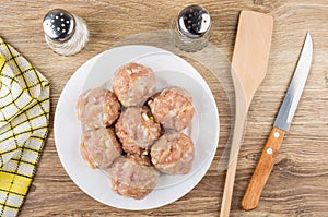 Raw meatballs in plate, spatula, salt, peeper and knife